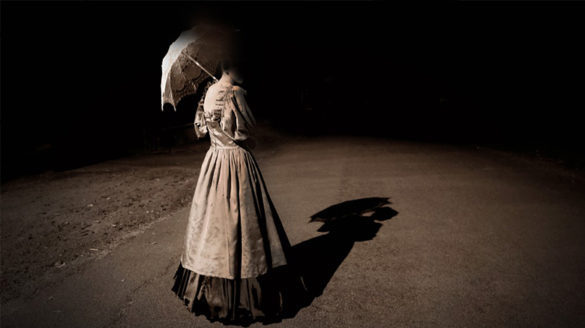 Ghostly woman holding umbrella on an ominous street.
