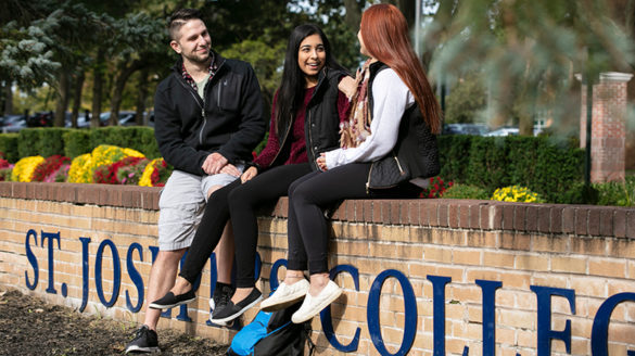 SJC Long Island students sitting on St. Joseph's College sign.