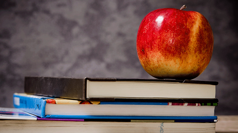 an apple on top of books stacked on a desk.
