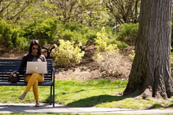 Woman seated on bench with laptop.