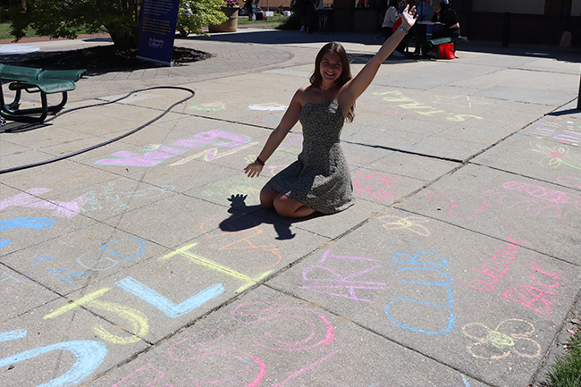 Cristina Costantino ’23, president of the Art Club, posing with sidewalk chalk art.