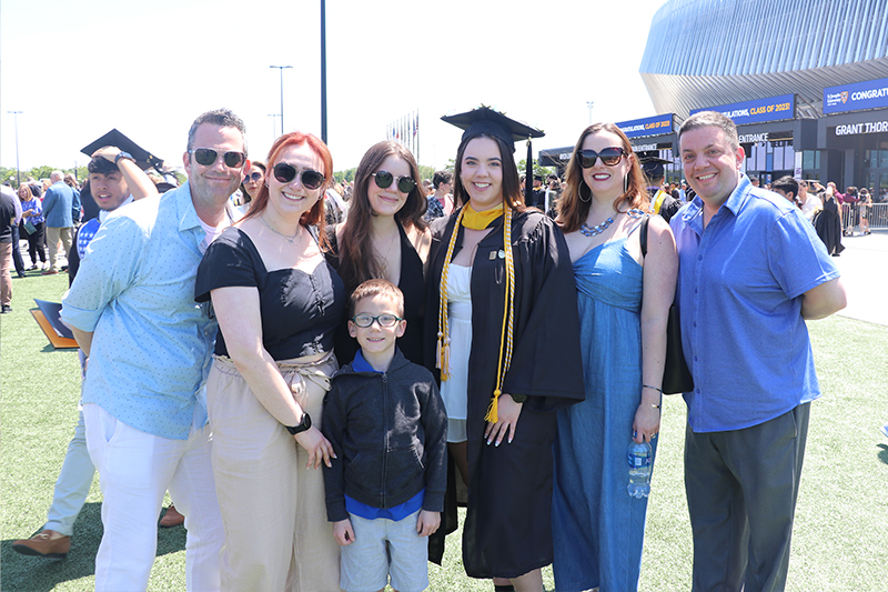 Student posing with family outside the coliseum at the Class of 2023 Commencement.