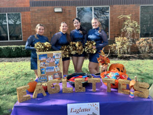 Four members of the Eaglettes smiling in uniform holding pom poms