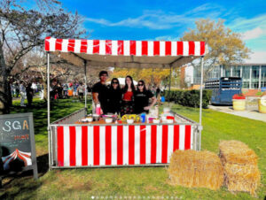 Four SGA members smiling in a red and white striped booth on a sunny day on campus